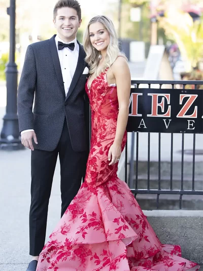 Man in a black diamond weave jacket and with a woman in a pink floral dress